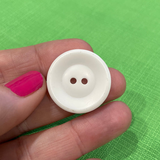 White button held between fingers on a green background