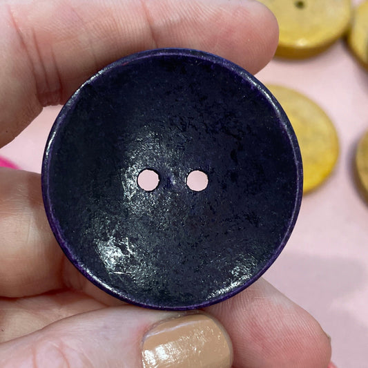 Hand holding a dark blue button with colorful buttons in the background