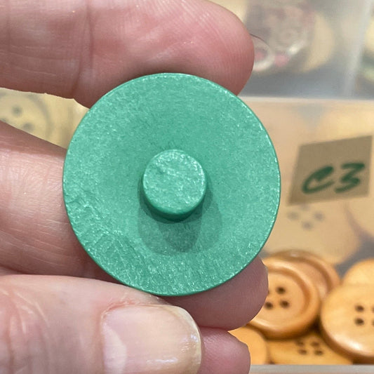 Hand holding a green button with a container of assorted buttons in the background