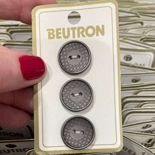 Three metallic buttons on a Beutron branded card held by a hand with red nail polish.