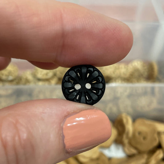 Black button held between two fingers with a container of assorted buttons in the background