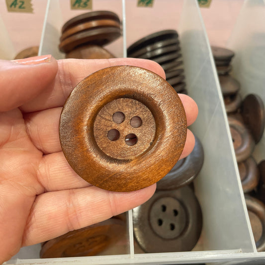 Hand holding a brown button with a blurred background of button display