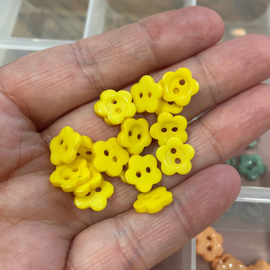 Hand holding yellow flower-shaped beads with a container of more beads in the background.
