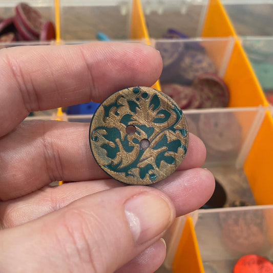 Hand holding a decorative button in front of a container with various buttons.