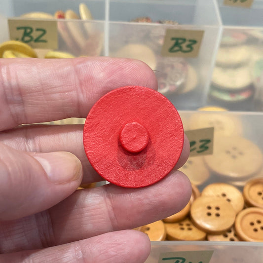 Hand holding a red button with a collection of buttons in a box in the background