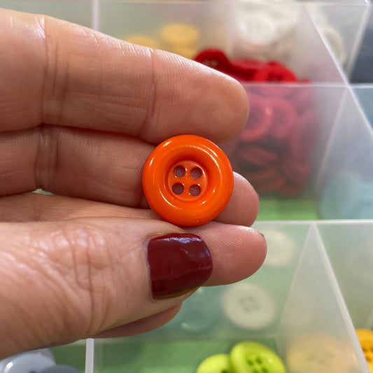 Hand holding an orange button with a container of colorful buttons in the background