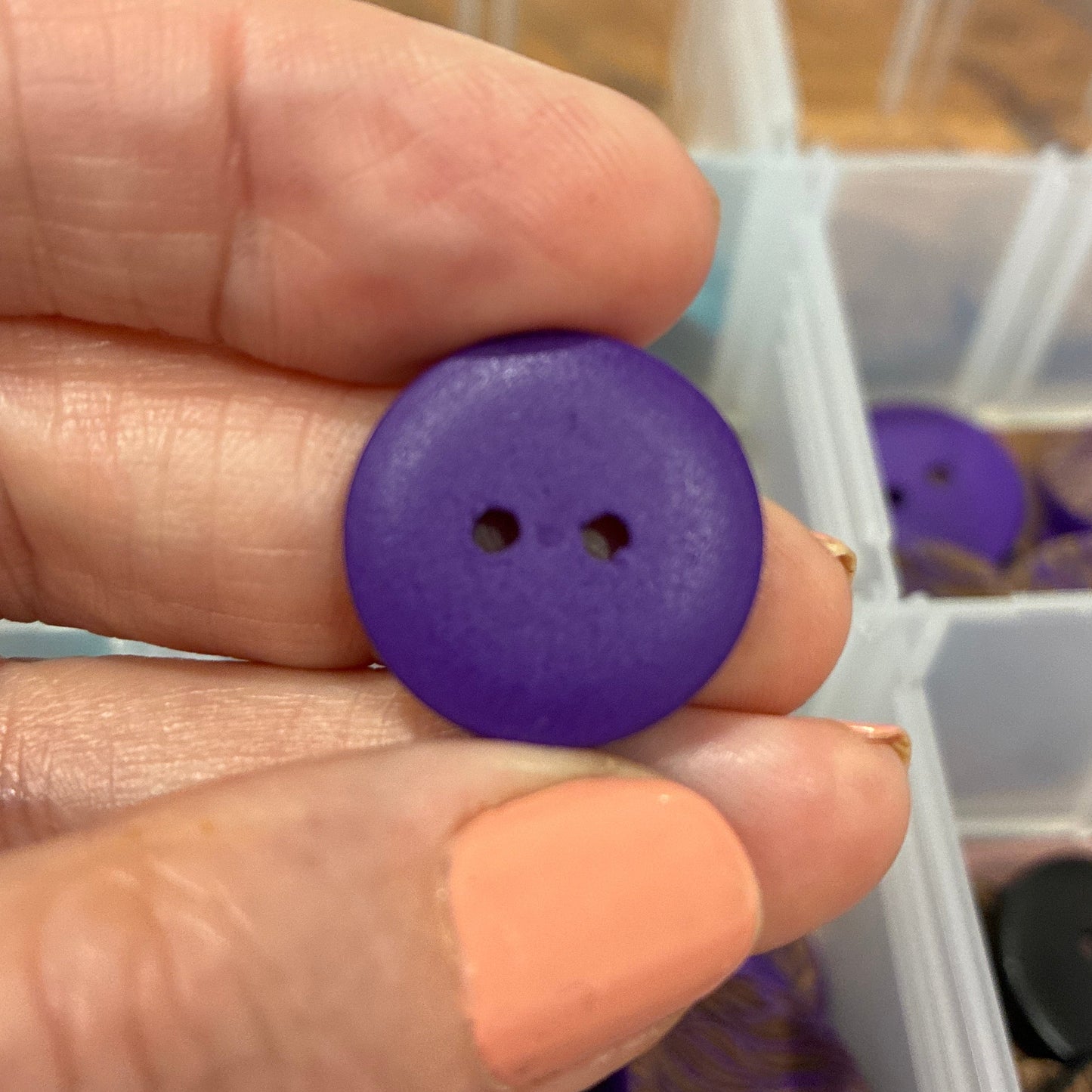 Hand holding a purple button with a container of buttons in the background
