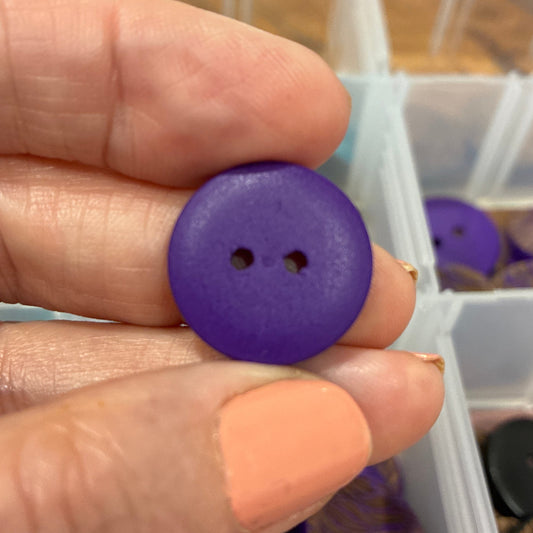 Hand holding a purple button with a container of buttons in the background