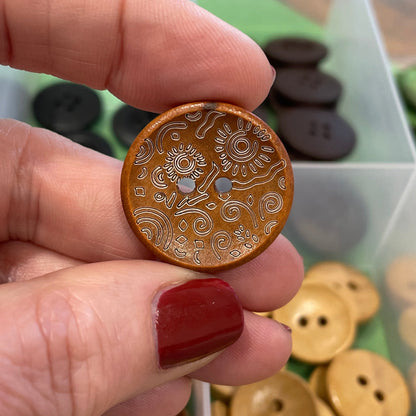 Hand holding a decorative button with a collection of buttons in the background