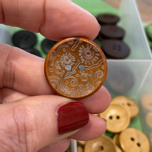 Hand holding a decorative button with a collection of buttons in the background