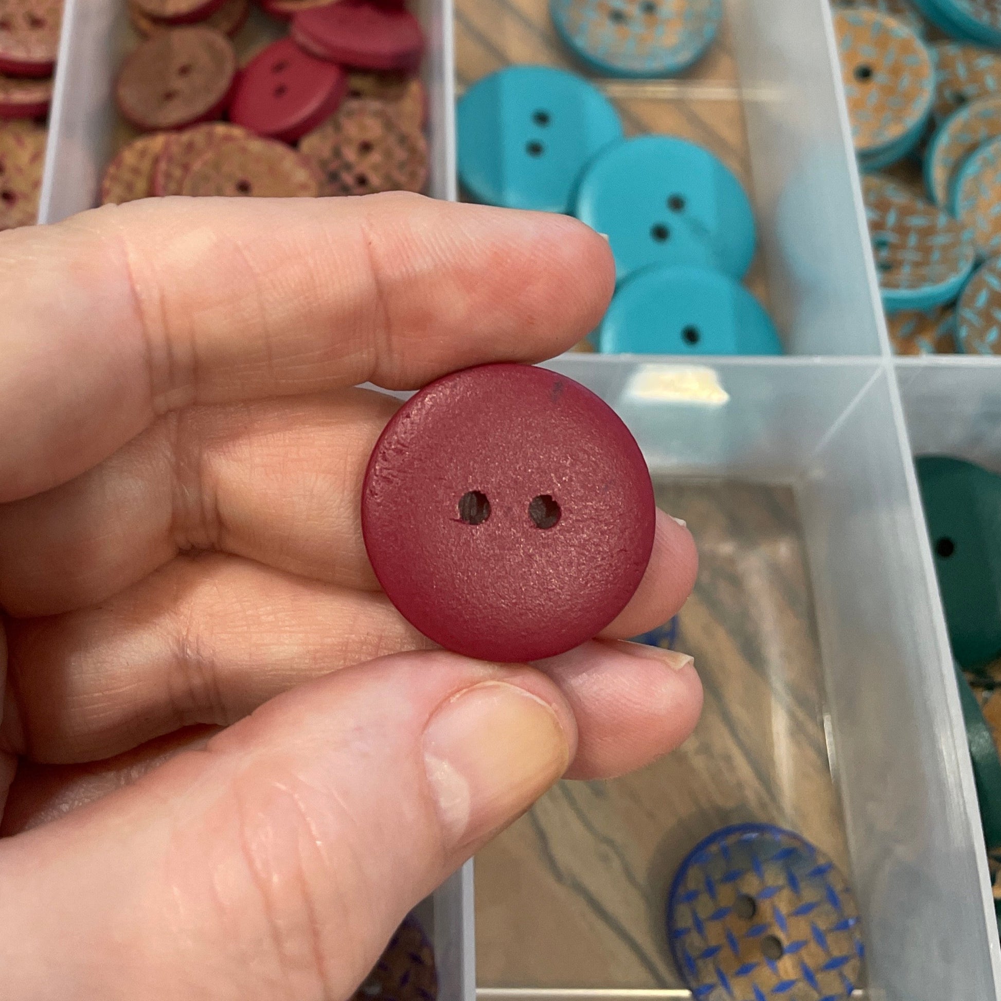 Hand holding a red button with a clear container of assorted buttons in the background