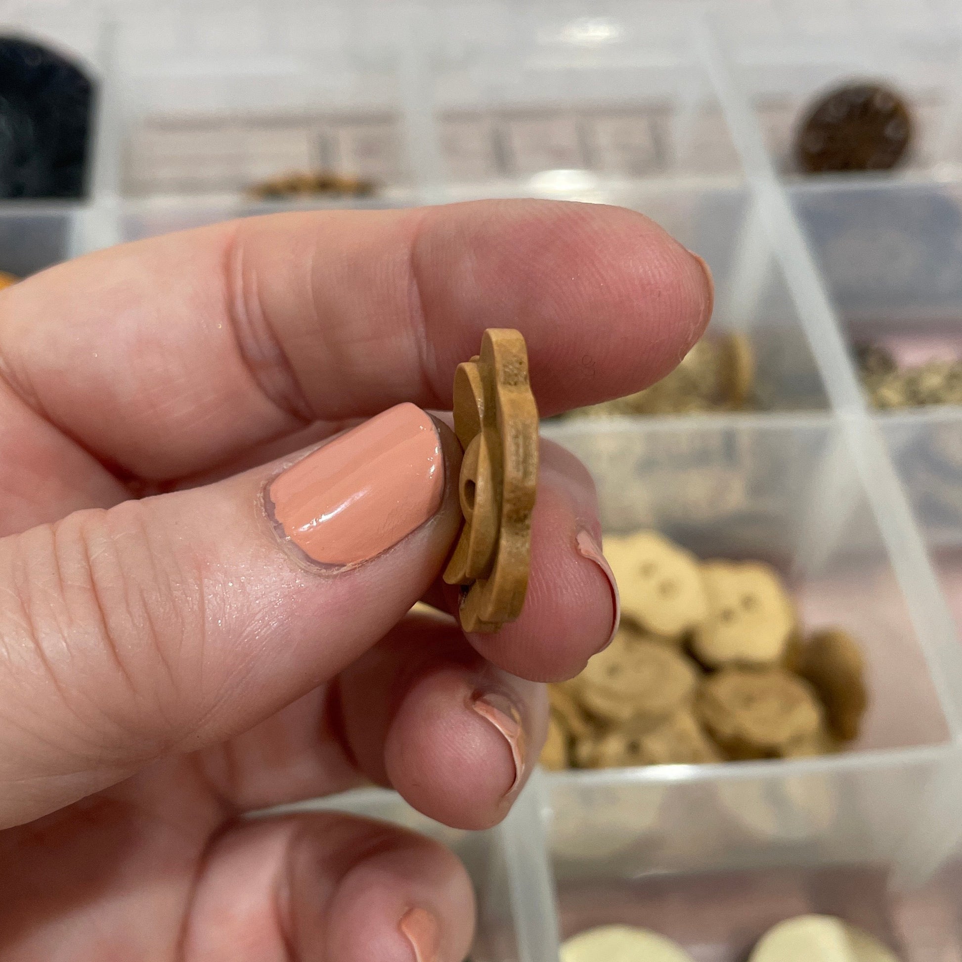 Hand holding a small gold button with a container of buttons in the background