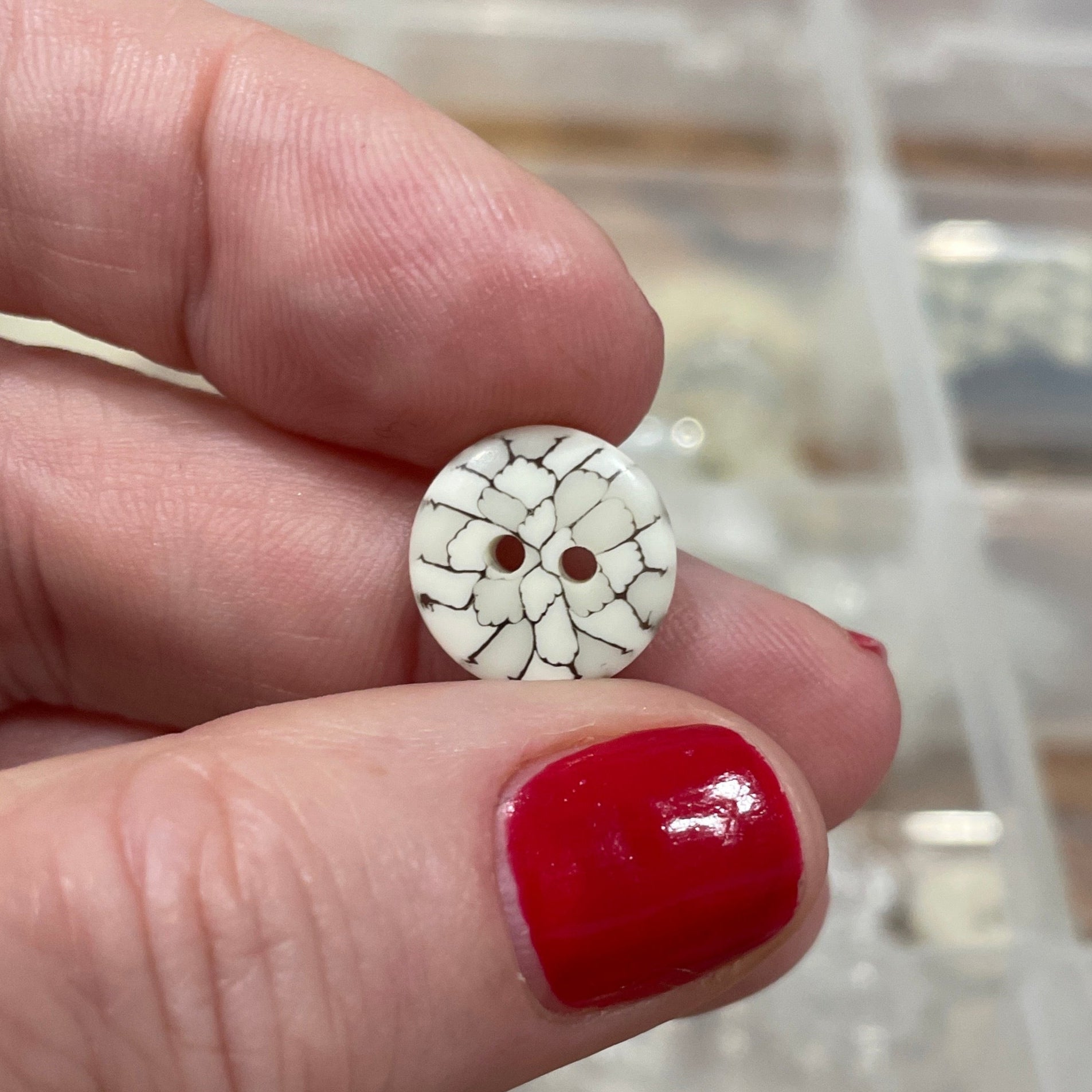 Hand holding a small round button with a blurred background of a button collection box.