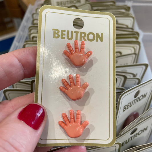 Three small hand-shaped buttons on a Beutron card held by a person with red nail polish.