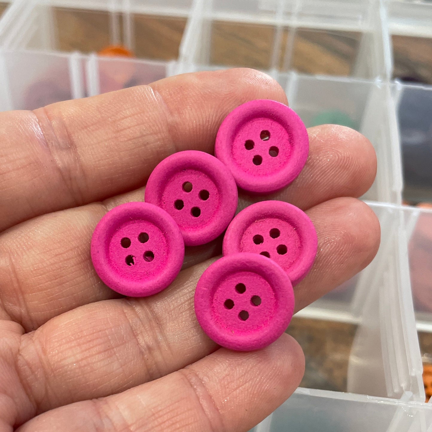 Pink buttons held in a hand with a container of buttons in the background