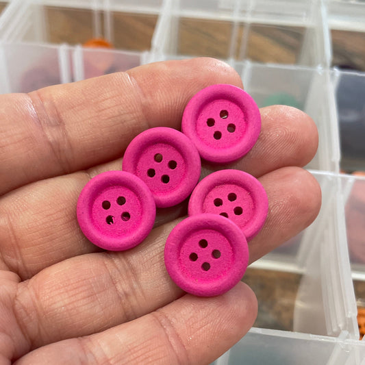 Pink buttons held in a hand with a container of buttons in the background