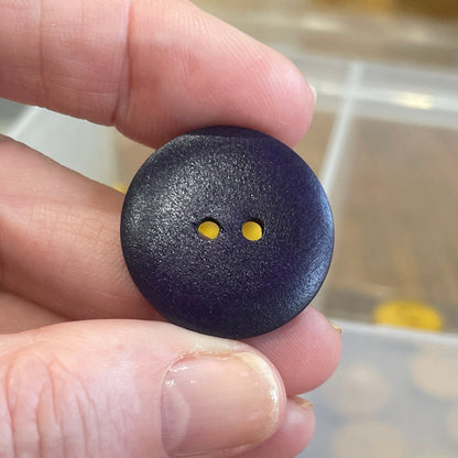 Hand holding a blue button with a blurred container of buttons in the background