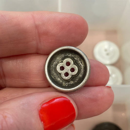 Hand holding a button with a clear container of buttons in the background