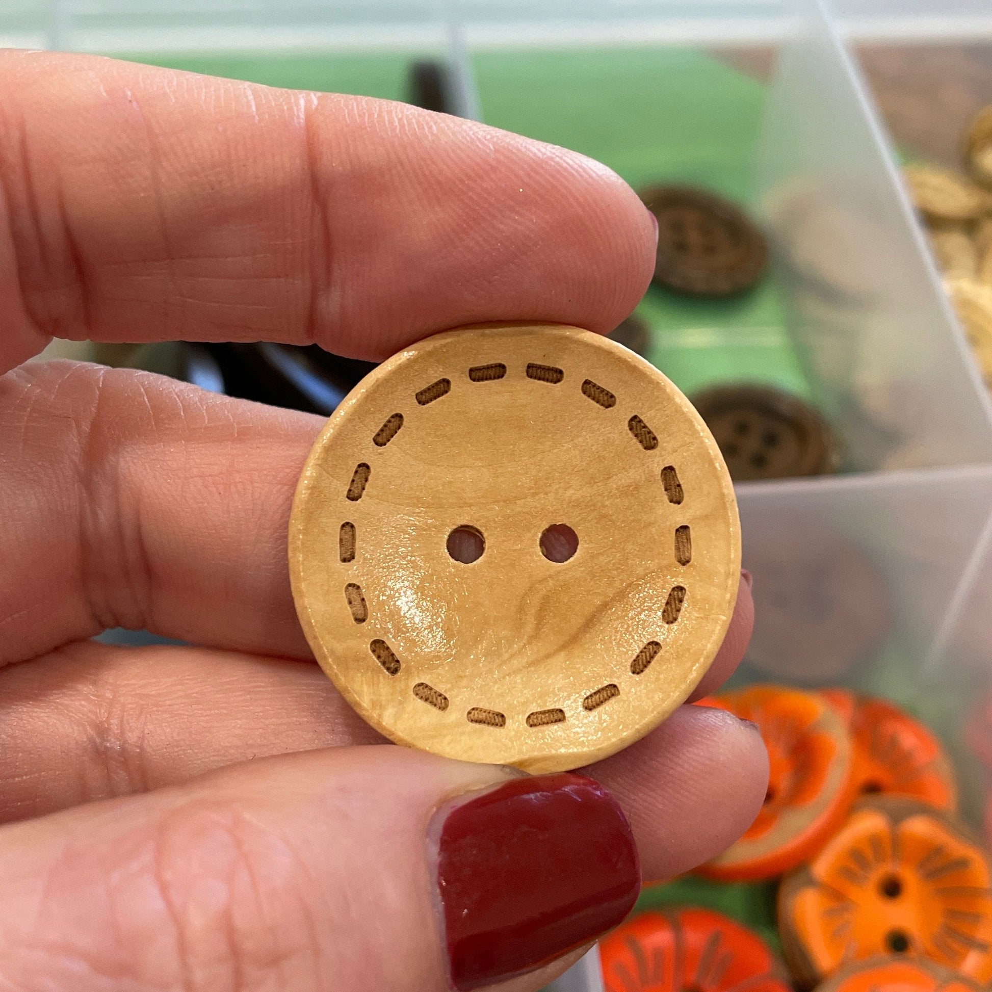 Hand holding a wooden button with a background of colorful buttons in a container.