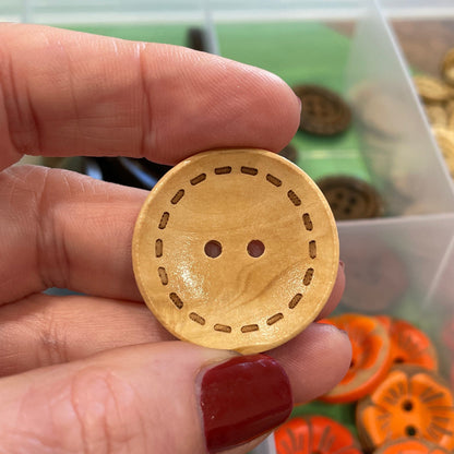 Hand holding a wooden button with a background of colorful buttons in a container.