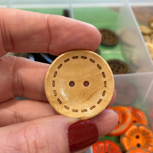 Hand holding a wooden button with a background of colorful buttons in a container.