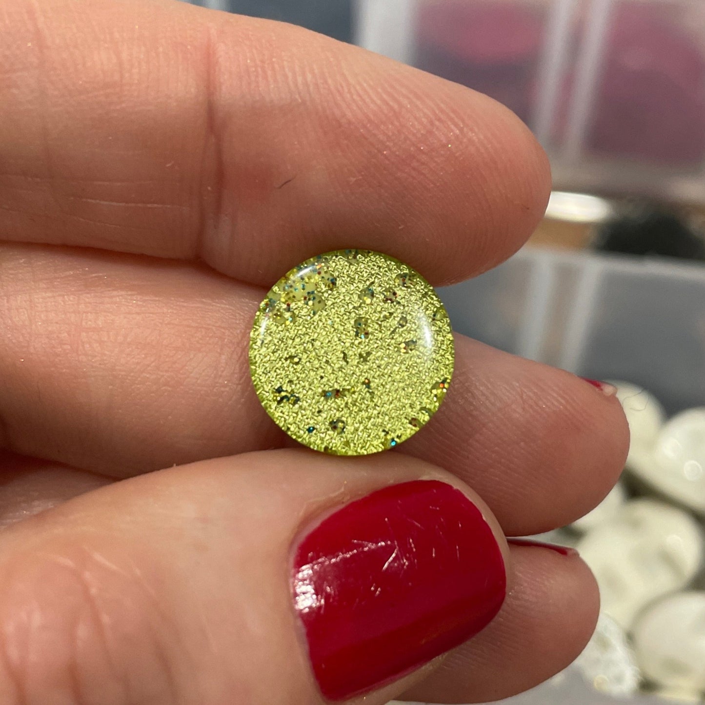Hand holding a yellow glittery earring with a blurred background of jewelry boxes.