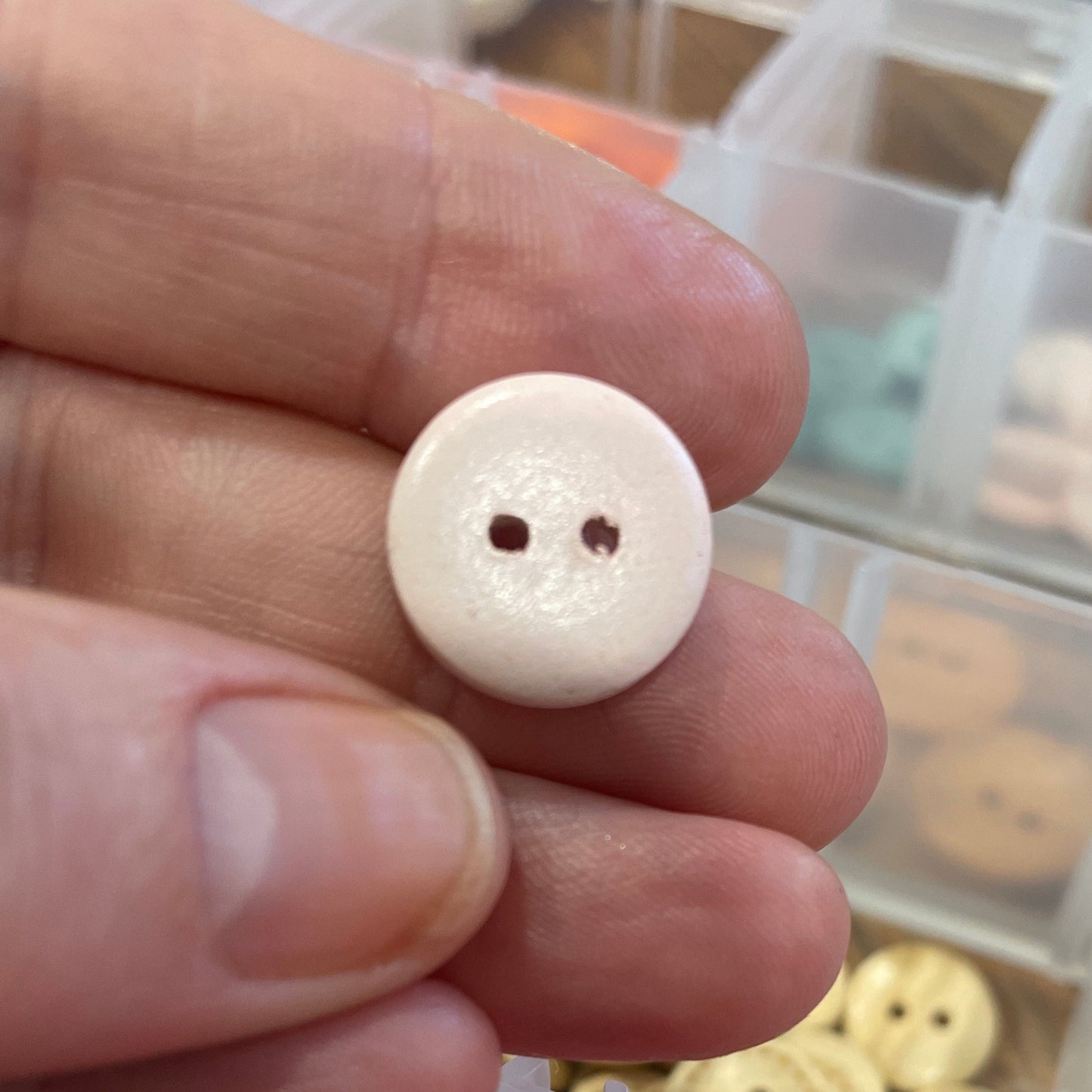 Close-up of a hand holding a white button with a container of pink buttons in the background.