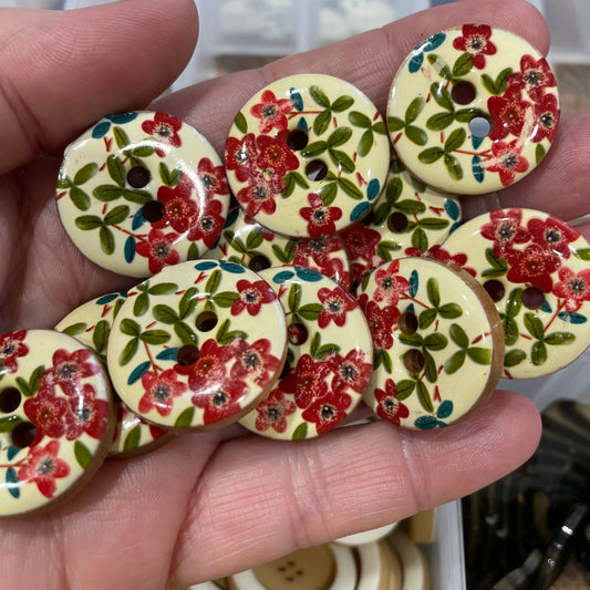Hand holding floral-patterned buttons with a clear container in the background