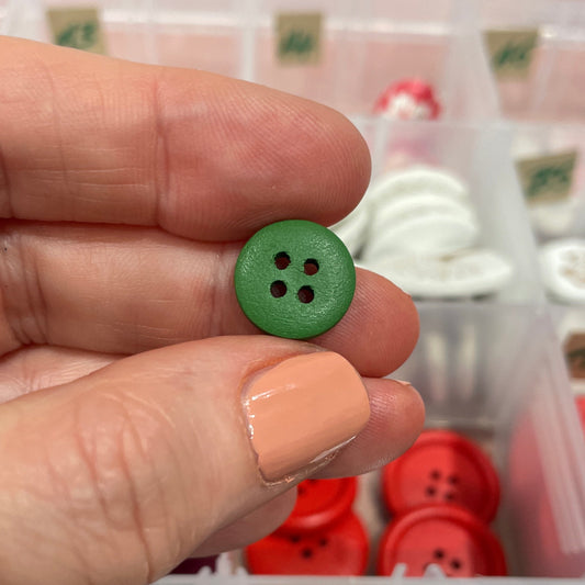 Hand holding a green button with a container of buttons in the background