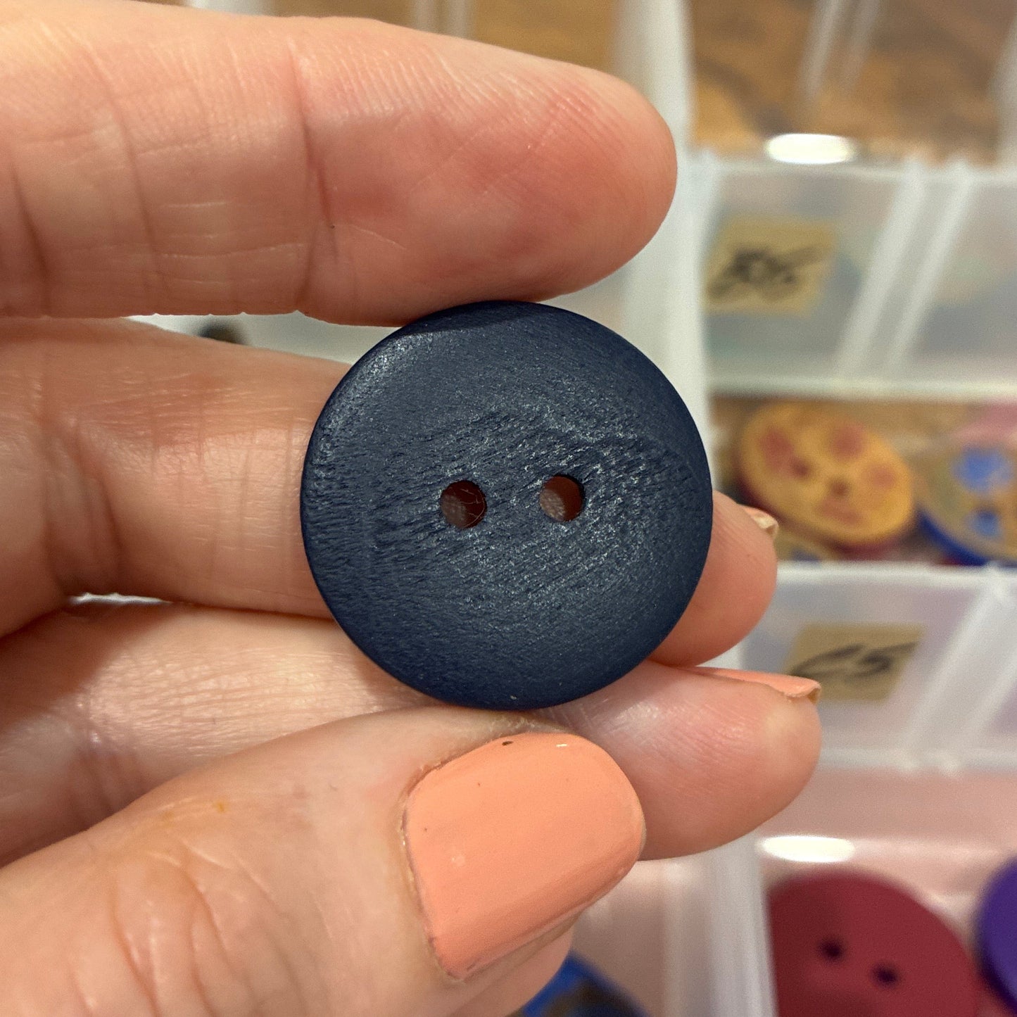 Hand holding a black button with a blurred background of a button collection organizer.