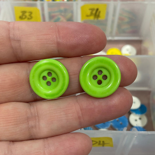 Green button held between fingers with a container of buttons in the background