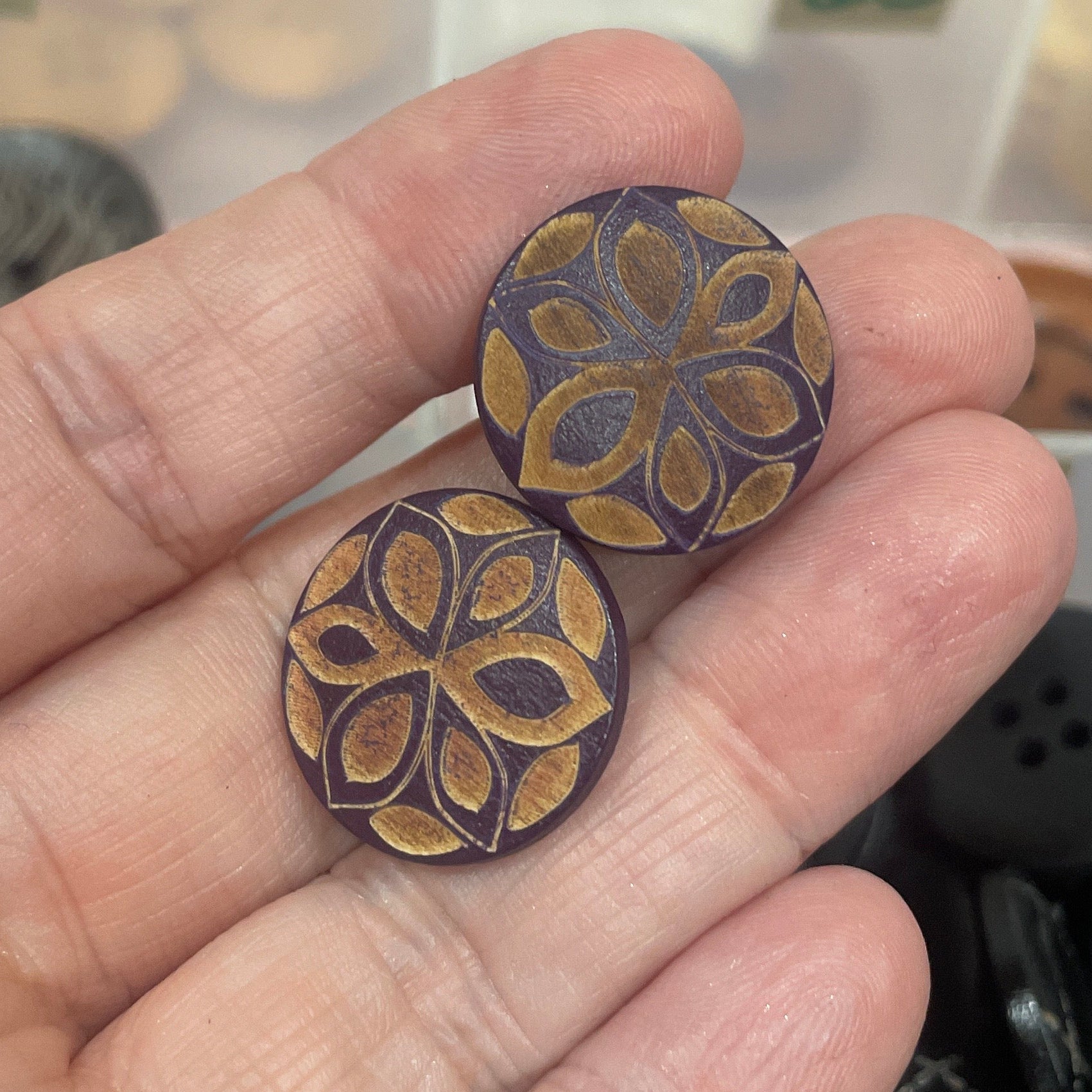 Hand holding two decorative buttons with a blurred background of button assortment.