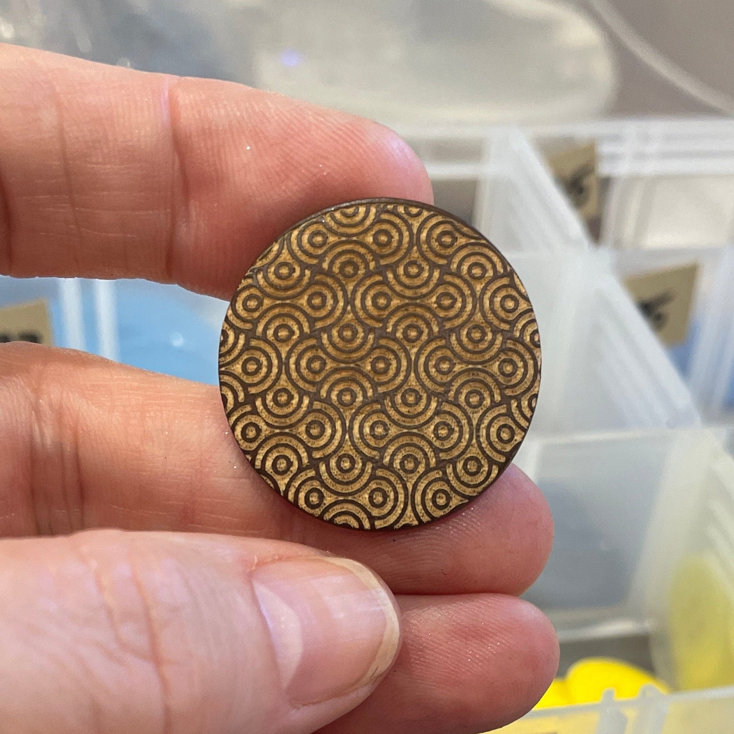 Hand holding a button with a pattern, surrounded by various colored buttons in a container.