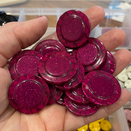 Hand holding pink glittery round objects with a blurred background of containers.