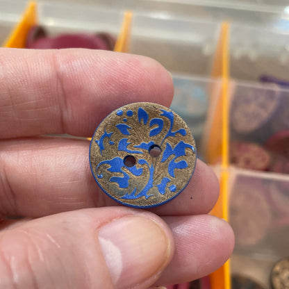 Hand holding a decorative button with intricate design, against a background of a button collection.