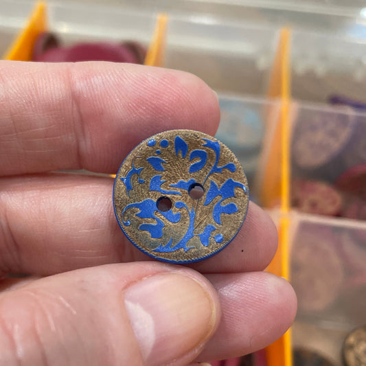 Hand holding a decorative button with intricate design, against a background of a button collection.