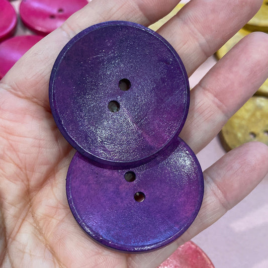 Hand holding two purple buttons with colorful buttons in the background