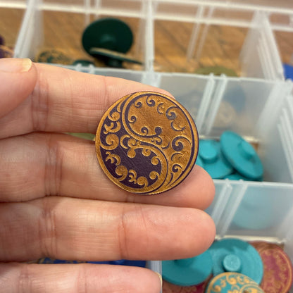 Hand holding a decorative button with a collection of similar buttons in the background.