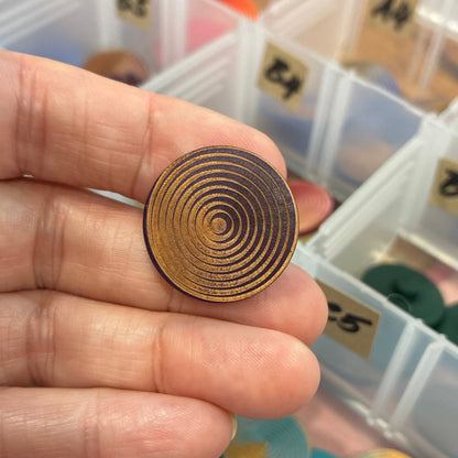 Hand holding a gold spiral button with a background of color swatches in a box.