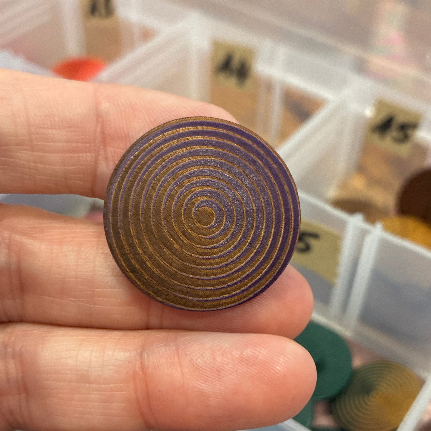 Hand holding a button with concentric circles against a background of color swatches.