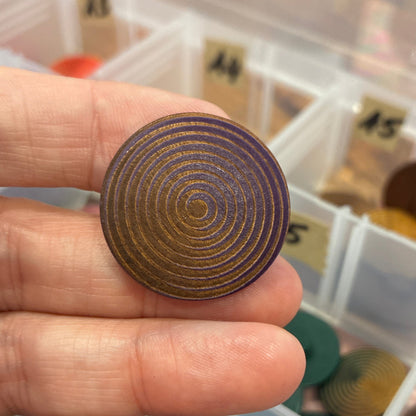 Hand holding a button with concentric circles against a background of color swatches.