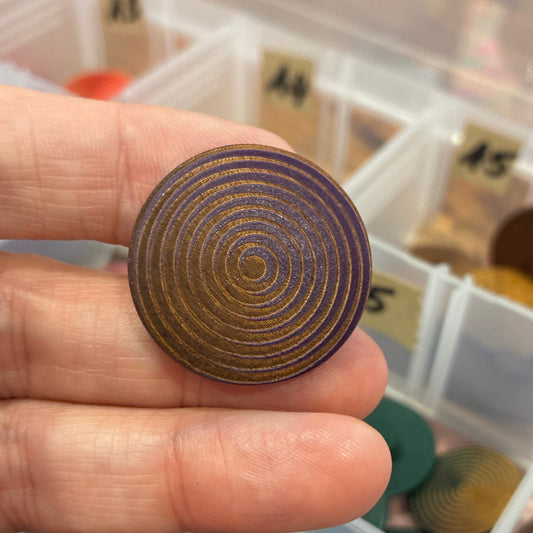 Hand holding a button with concentric circles against a background of color swatches.