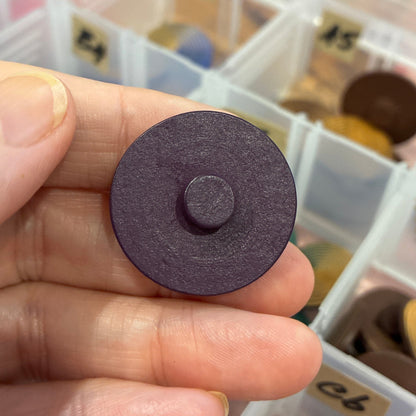 Round purple button held in hand with button organizer in background