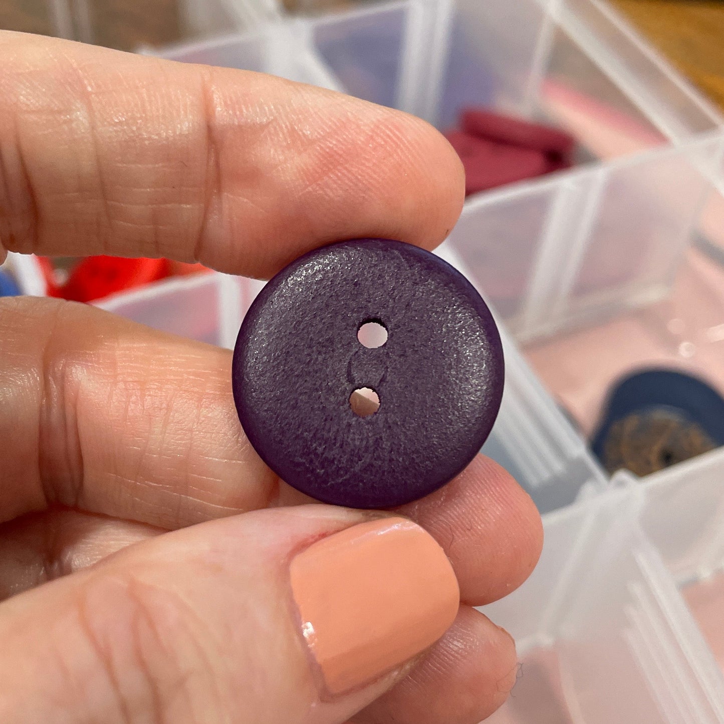 Hand holding a purple button with a container of buttons in the background