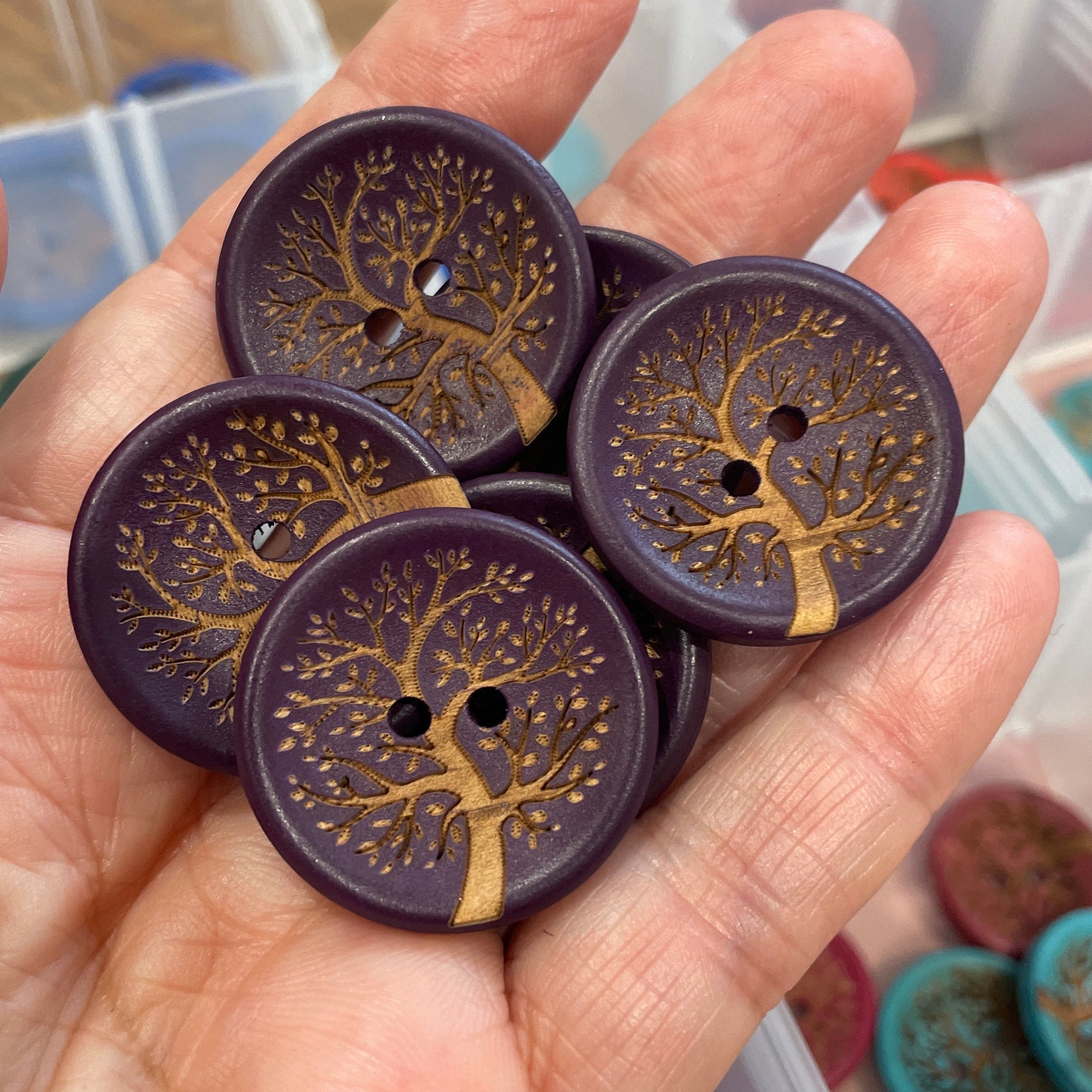Hand holding purple buttons with gold tree designs, container of buttons in the background