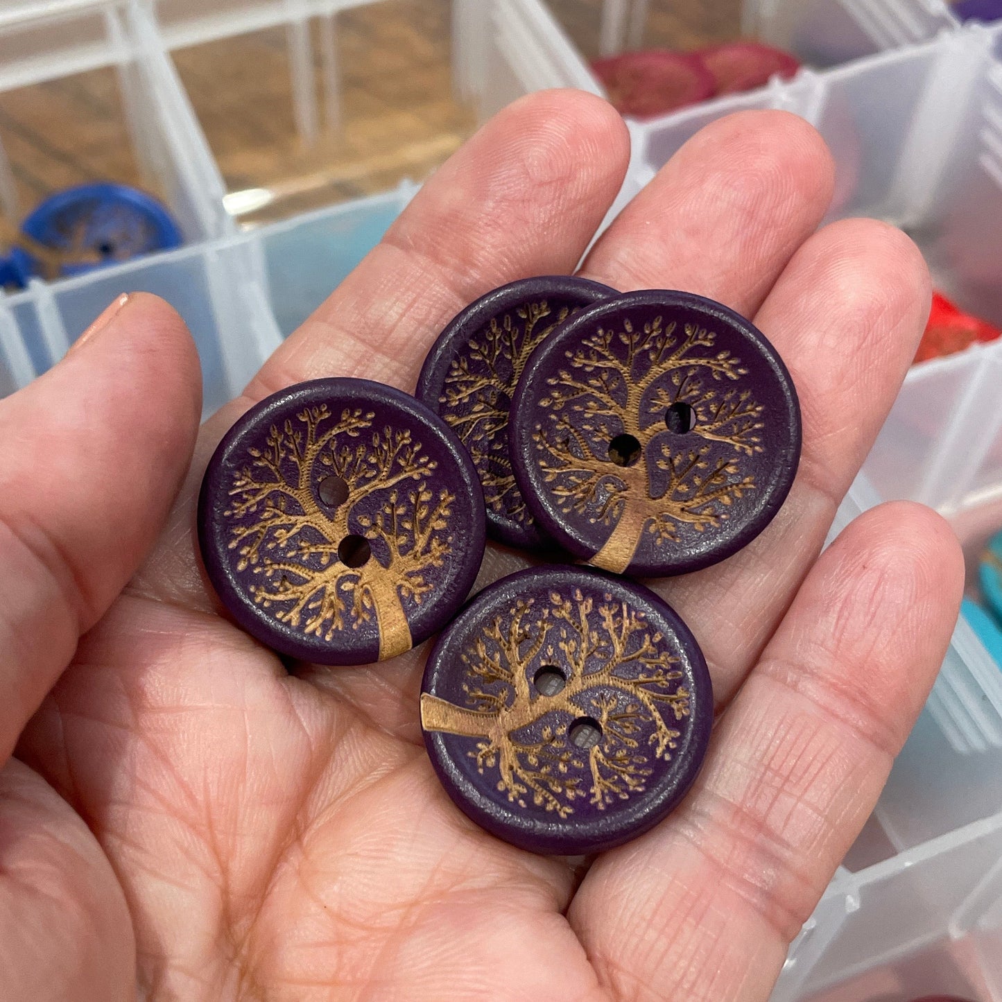 Hand holding decorative buttons with intricate designs, with a blurred background of a container.