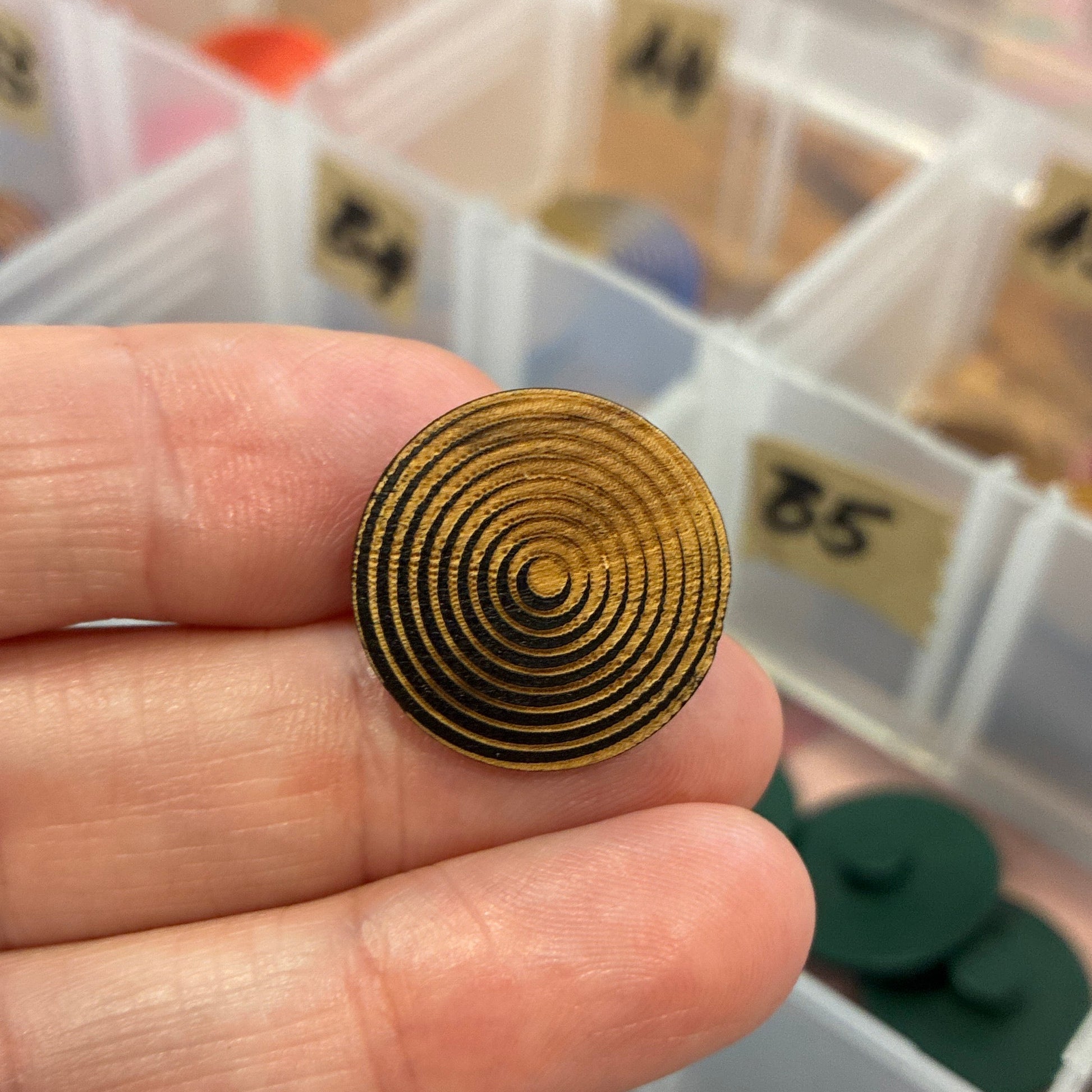 Gold spiral button held between fingers with a clear plastic organizer in the background.