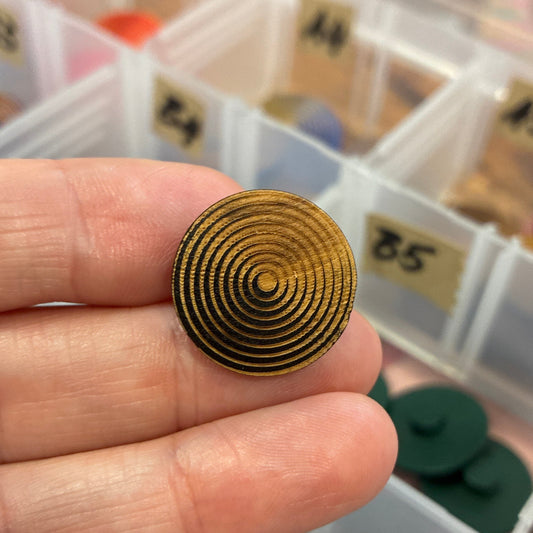 Gold spiral button held between fingers with a clear plastic organizer in the background.