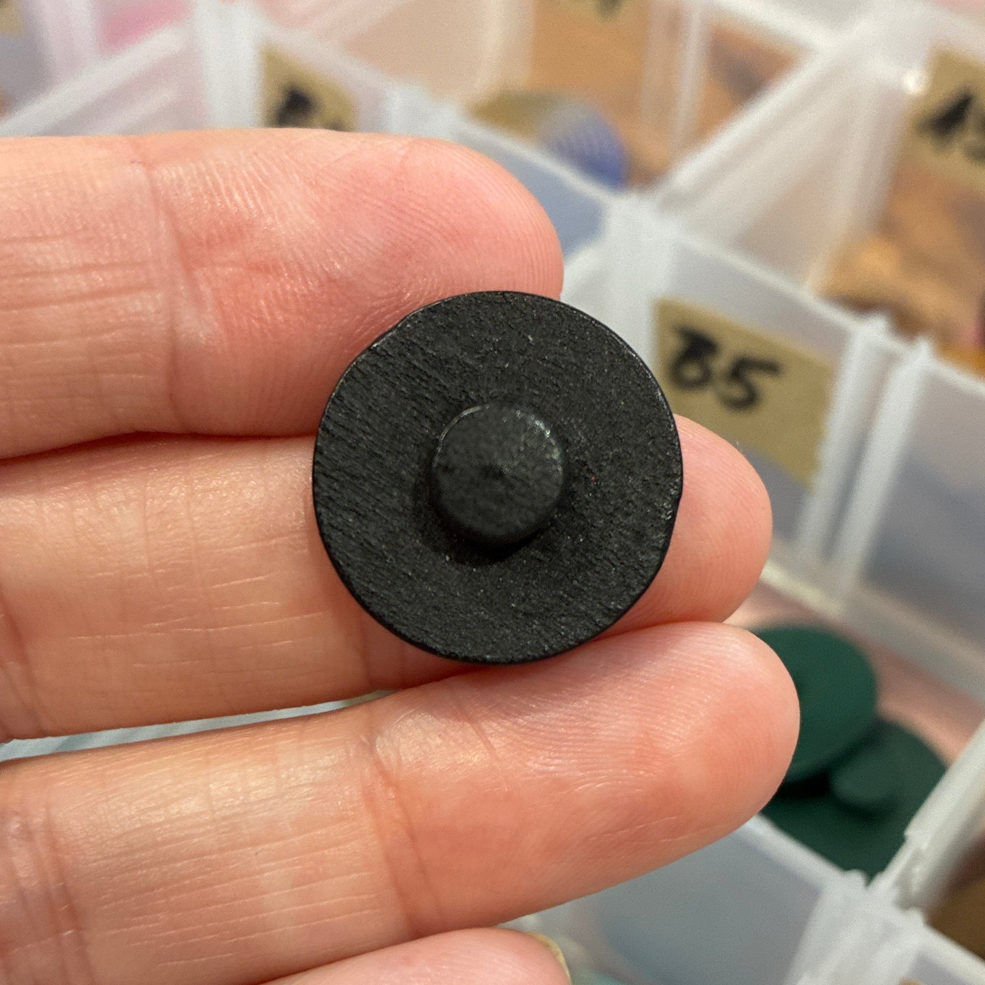 Hand holding a black button with a collection of colorful buttons in the background