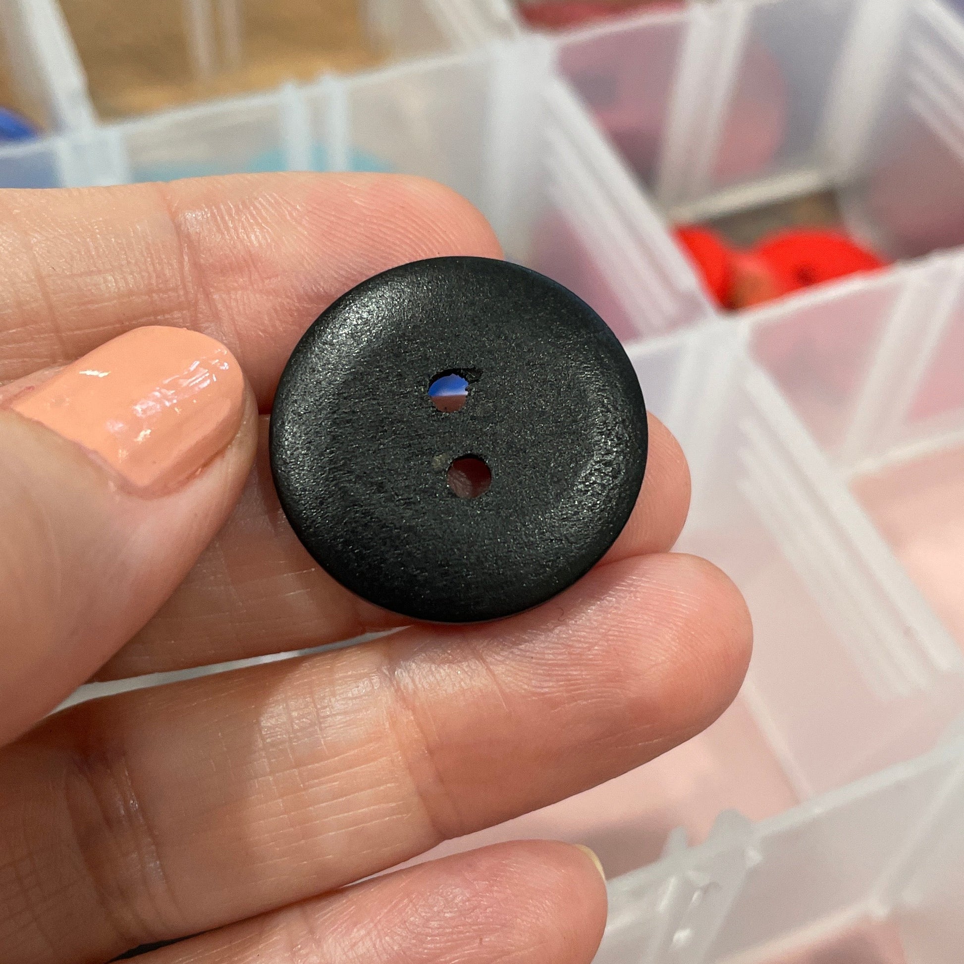 Black button held in a hand with a container of colorful buttons in the background